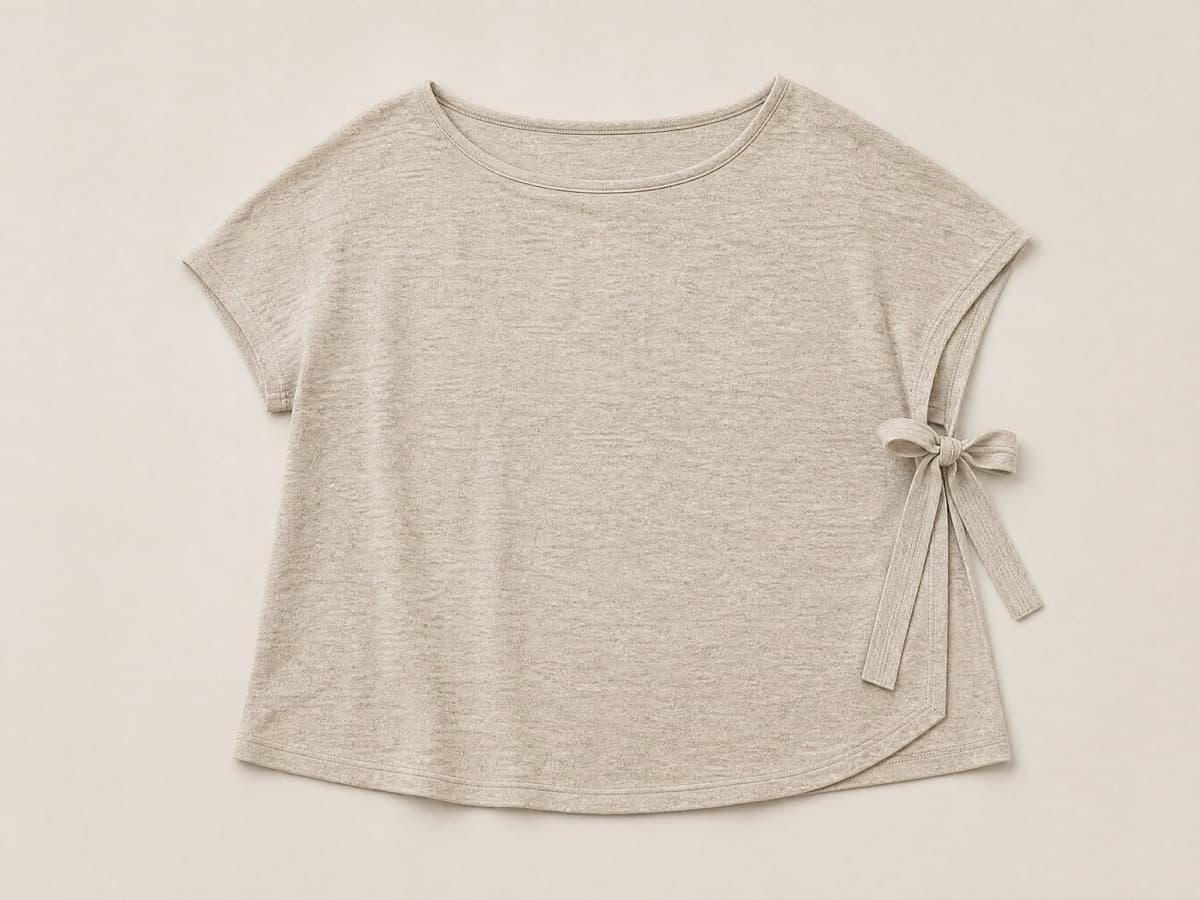 A soft sand jersey pull-on top laid flat with no buttons and no zips, and two wide flat cotton tapes at one side seam loosely tied.