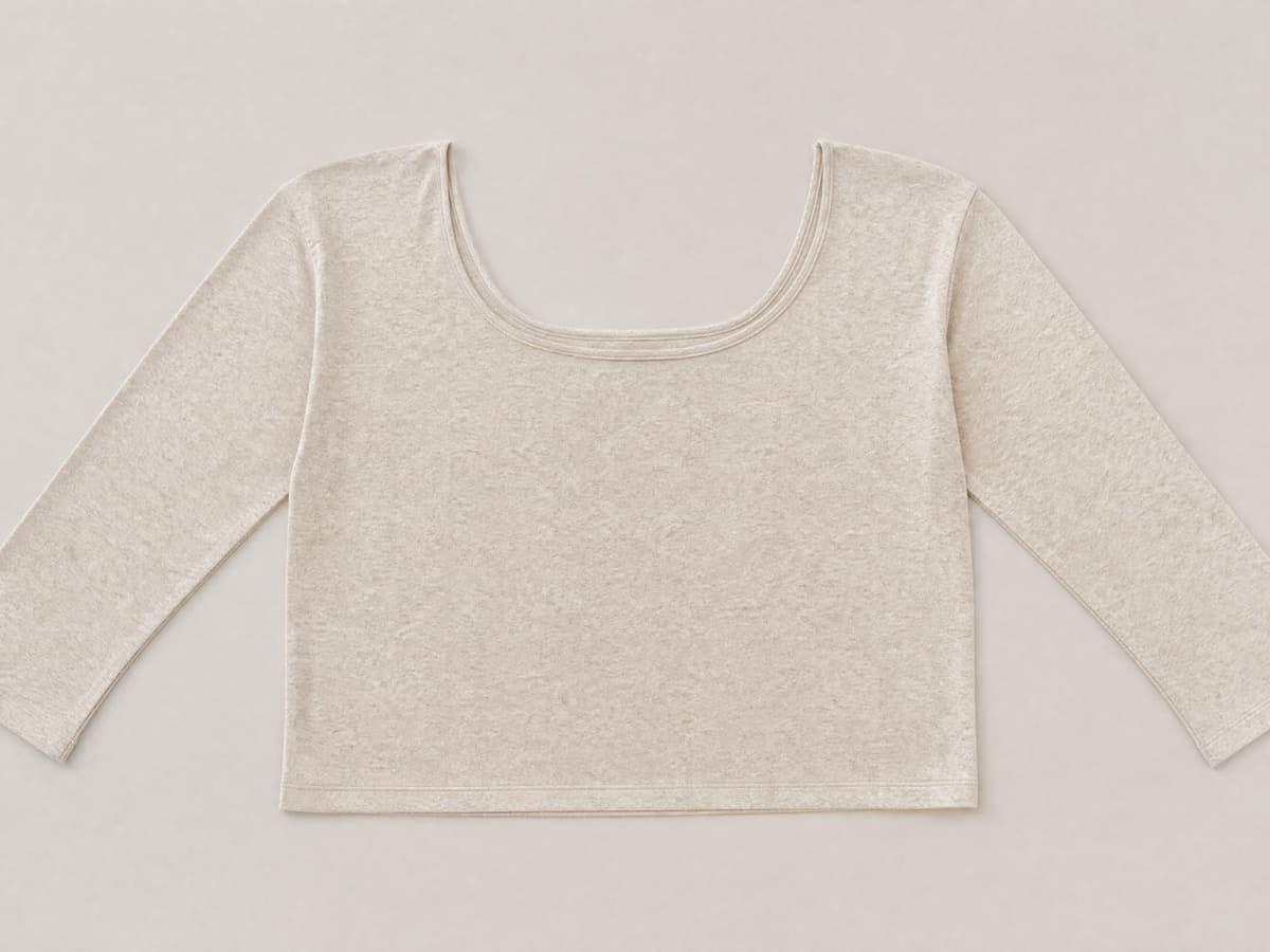 An oatmeal jersey long-sleeve top laid flat with an unusually wide relaxed neckline and long straight sleeves laid out to the sides.